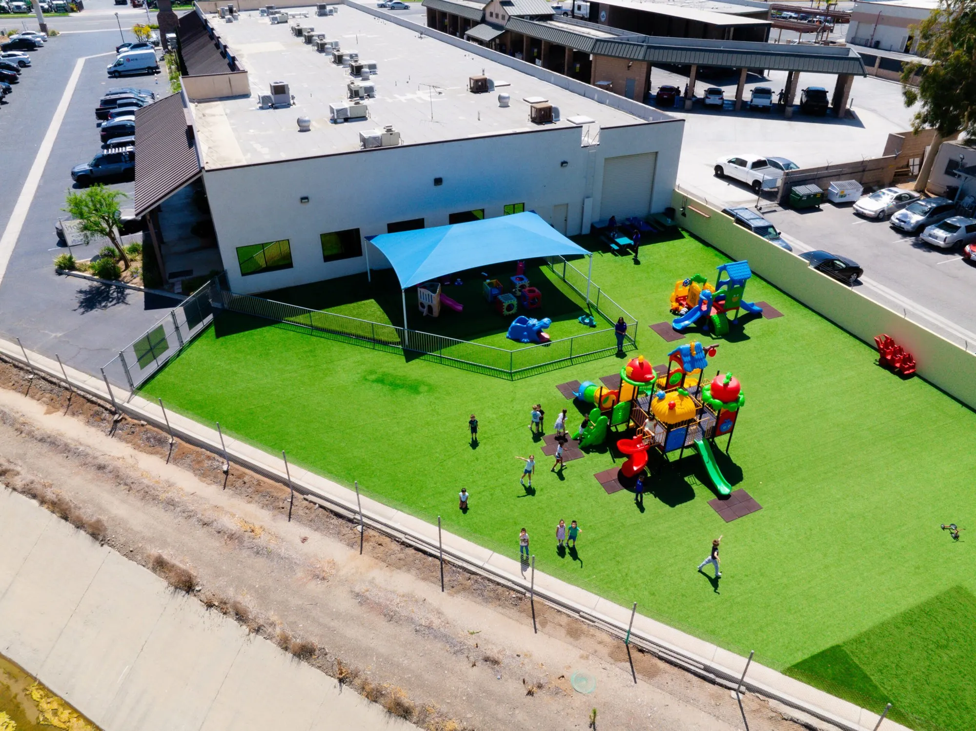 Aerial view of the Norco Montessori Academy building with its fenced turf playground and shade canopy.