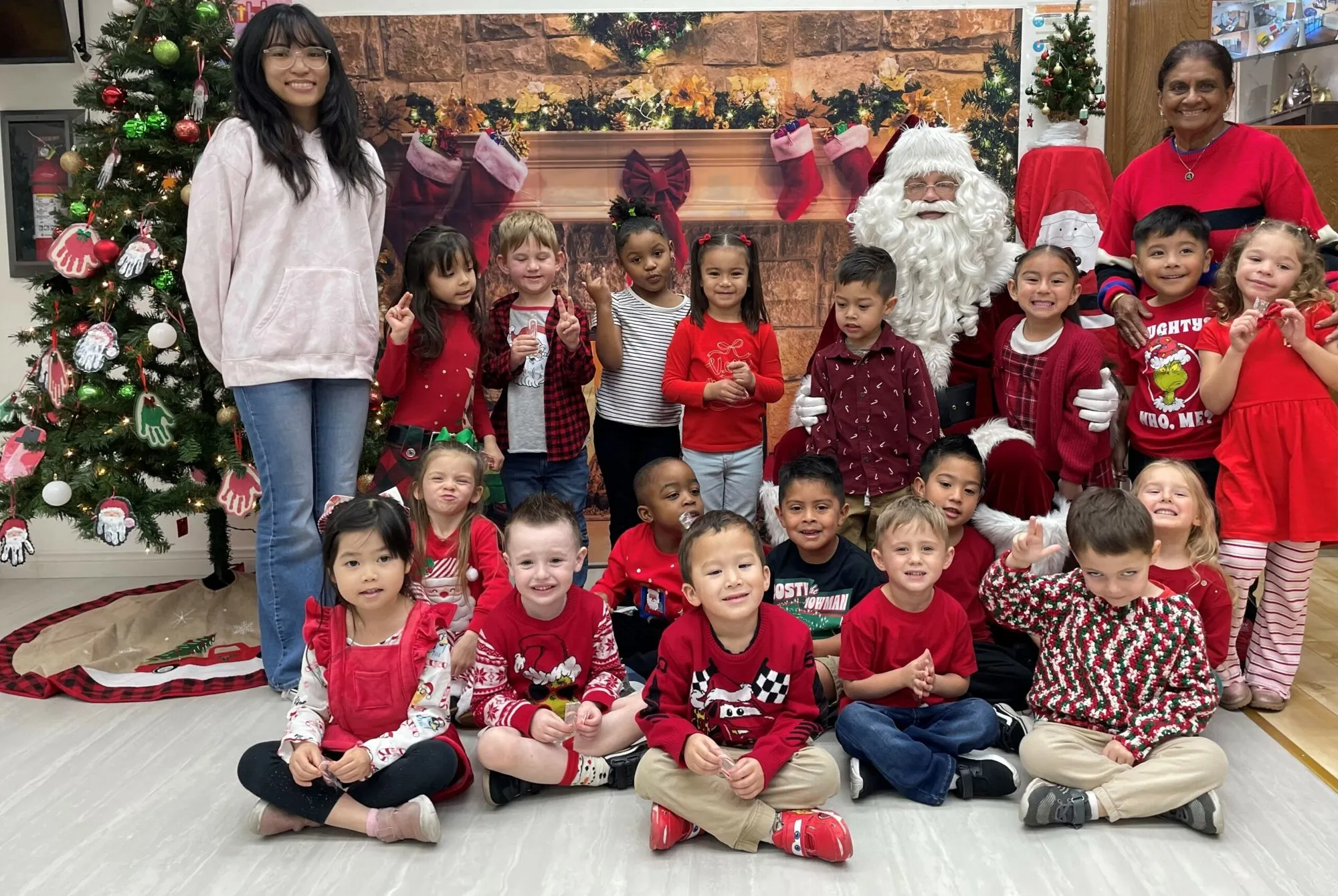 Students and teachers gather around Santa beside a decorated tree during a holiday visit at school.